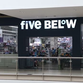 Five Below - The photo captures the storefront of Five Below, a discount retail store, located inside a shopping mall. The store's sign, displaying 'five BELOW' in large, illuminated letters, is prominently positioned above the entrance. The interior of the store is visible through the glass, showing shelves stocked with various products, and a few shoppers browsing inside. The mall corridor in front of the store features a glass railing and a clean, modern design. - Accessories Near Me - West Nyack, New York