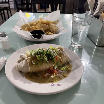The 377 Brewery - Bean and cheese burrito and chips and salsa - A restaurant table features a burrito with lettuce and salsa, a side of chips with salsa, and a glass of water, with restaurant staff visible in the background. - Brewpubs Near Me - Albuquerque, New Mexico