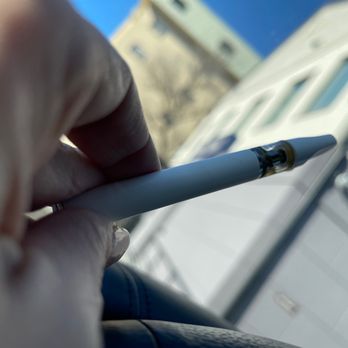 Union Twist - 1/3 full cartridge - A hand holding a white pen with a transparent tip is visible, with an outdoor scene and buildings blurred in the background. - Cannabis Dispensaries Near Me - Framingham, Massachusetts