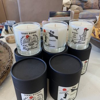 Luna and Luz - Candles - Three candles in glass containers with labels featuring illustrations and text, set on black cylindrical boxes on a table. - Jewelry Near Me - Albuquerque, New Mexico