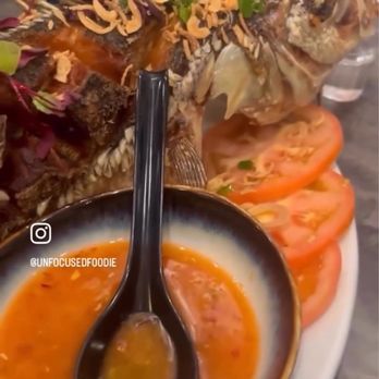 Dan Da - A whole fish garnished with herbs and fried shallots is presented with sliced tomatoes, a bowl of dipping sauce, and beverages on a table. - Vietnamese Near Me - Aurora, Colorado