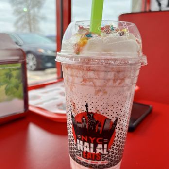 NYC Halal Eats - Fruity Pebbles Milkshake - A pink and white Fruity Pebbles milkshake with sprinkles in a clear plastic cup with a green straw, on a red table at NYC Halal Eats. - Halal Near Me - Indianapolis, Indiana