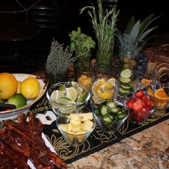 933 Speakeasy - Garnish station for cocktails - A garnish station for cocktails features fresh fruits, herbs, and vegetables in glass bowls and containers on a bar counter, with a marble surface. - Speakeasies Near Me - Lockport, Illinois