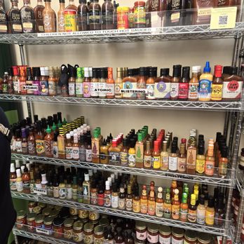The Big Cheese - Everything hot! - A metal shelving unit holds a variety of hot sauces, seasonings, and condiments in bottles and jars. The top shelf contains larger bottles with labels, while the lower shelves feature smaller bottles and jars, organized by type and brand. The setting appears to be a retail store or storage area for hot sauce products. - Cheese Shops Near Me - Annapolis, Maryland