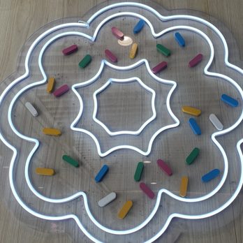 T% Coffee + Tea - Davis  - A neon light in the shape of a flower with multiple layers, containing colorful pill-shaped objects on a wooden surface. - Bubble Tea Near Me - Davis, California