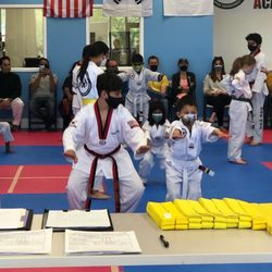 JTA Jeong Jaehyun Taekwondo Academy - A high belt supports a color belt with doing squats during an exam.