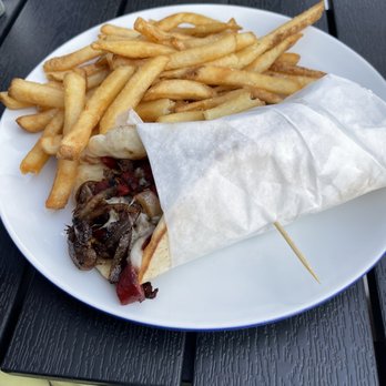 Evie’s - A white plate holds French fries and a wrapped sandwich with mushrooms and red peppers, placed on a dark outdoor table. - Beer, Wine & Spirits Near Me - Westerly, Rhode Island