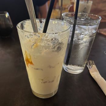 Holy Burgers - Heavenly Milkshake - A milkshake with remnants of caramel and pretzel pieces, served in a tall glass with two straws, on a dark table at a casual restaurant. - Burgers Near Me - Albuquerque, New Mexico