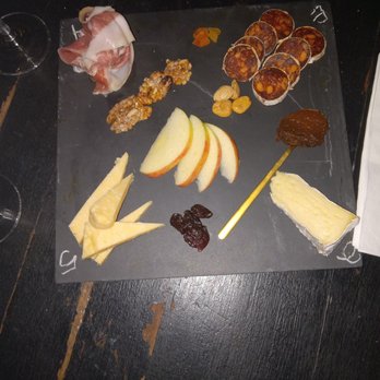 The Esters - The lovely Cheese and Meat Board - A cheese and meat board featuring sliced apples, nuts, dried fruit, cheese, and small cups of spreads or sauces, arranged on a black slate. - Cocktail Bars Near Me - Brooklyn, New York
