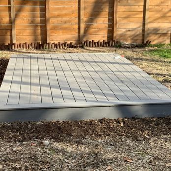 Red Knights Construction - A standalone, rectangular deck platform constructed with grey composite boards, built low to the ground near a wooden fence... - Decks & Railing Near Me - Cedar Creek, Texas Red Knights Construction - A standalone, rectangular deck platform constructed with grey composite boards, built low to the ground near a wooden fence... - Decks & Railing Near Me - Cedar Creek, Texas