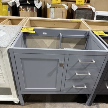 Seconds & Surplus - This model didn't include the sink or countertop. - A gray bathroom vanity with a cabinet door and three drawers, displayed in a store with price tags. The vanity lacks a sink and countertop. - Building Supplies Near Me - Richardson, Texas