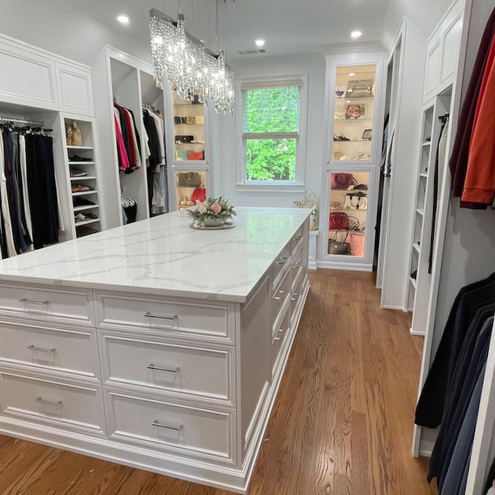 Best Price Custom Cabinets - Master closet - wide view showing the two storage walls, center island, two illuminated cabinets flanking window - Building Supplies Near Me - Cumming, Georgia Best Price Custom Cabinets - Master closet - wide view showing the two storage walls, center island, two illuminated cabinets flanking window - Building Supplies Near Me - Cumming, Georgia
