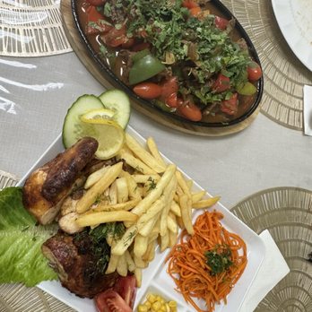 Caravan Restaurant - Jarovnya and Chicken Tabaka - A meal includes grilled meat with lemon and cucumber slices, French fries, shredded carrots, and various vegetables and condiments, served on a white plate. - Uzbek Near Me - Bolingbrook, Illinois