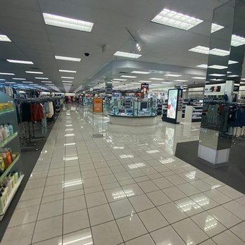 Kohl's - The image shows a large retail store interior with a tiled, reflective floor and bright overhead lighting. Clothing displays and accessories are arranged along the sides and center of the store, with digital screens and signage visible. The store appears organized and spacious, with a few customers visible in the distance. - Department Stores Near Me - ORLAND PARK, Illinois