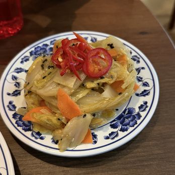 Woon - A dish of pickled vegetables, including cabbage and carrots, topped with sliced red chili peppers, served on a decorative blue and white plate. - Chinese Near Me - Pasadena, California