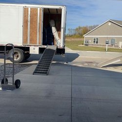 TopDogg Moving - Two moving trucks parked in a driveway with ramps extended. A dolly is placed on the concrete, and furniture is being unloaded.