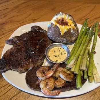 Outback Steakhouse - Ribeye* 13 oz. - A meal featuring a grilled steak, shrimp, baked potato with toppings, and asparagus on a white plate at Outback Steakhouse. - Steakhouses Near Me - Slidell, Louisiana