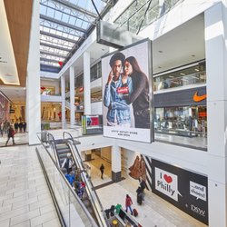 Fashion District Philadelphia - Multi-level interior of Fashion District Philadelphia with shoppers, escalators and a large digital display.