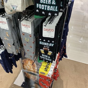 Boscov's - A retail display features socks with sports and beer-themed designs, including phrases like 'Sunday is for Beer & Football.' The socks are hung on hooks on a metal rack, with various other socks visible nearby. The store has a light-colored floor and a reflective metal base at the bottom of the display. - Department Stores Near Me - Rochester, New York