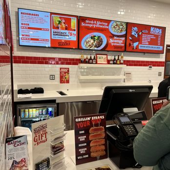 Sizzler - Counter - Digital menu screens at Sizzler in Merced, CA, show food items like steak, shrimp, and scampi, along with beverages and kid's meals. - Seafood Near Me - Merced, California