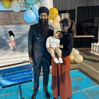 Amasingh Magic - A man wearing a turban and a woman holding a child stand together at an event with balloon decorations and a lit dance floor. - Magicians Near Me