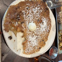 Carrot cake pecan pancake - A large carrot cake pecan pancake with powdered sugar and a dollop of butter on top, served on a white plate at a restaurant.