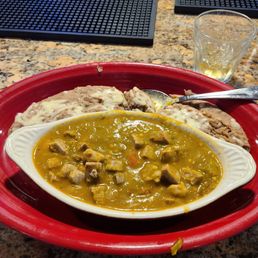 Green chile pork - A red tray holds a dish of green chile pork with rice and beans, on a granite countertop at a restaurant.