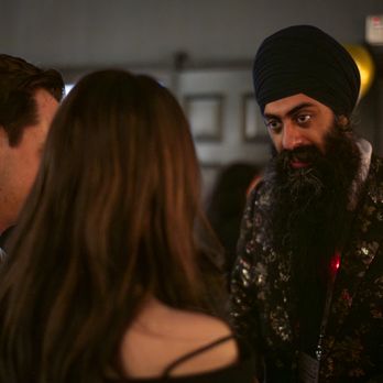 Amasingh Magic - A man with a turban and a patterned jacket engages in conversation with two individuals at an indoor gathering. - Magicians Near Me