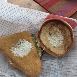 Arby's new fish sandwich - A fish sandwich with a breaded fillet, lettuce, and tartar sauce is served in a bread bowl, placed on paper with a wooden table background.