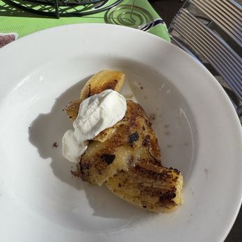 Tune-Up Cafe - Fried banana with dollop of sour cream crema - A white plate holds a grilled banana with visible grill marks, topped with a dollop of sour cream. The plate is placed on a green tablecloth, with outdoor seating and a wire basket visible in the background, indicating an outdoor dining setting. - New Mexican Cuisine Near Me - Santa Fe, New Mexico