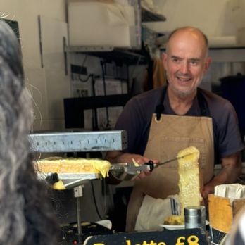 Kappacasein - Employee at Kaapcasein in Borough market scraping melted cheese from the raclette onto cooked potatoes. - Cheese Shops Near Me - London, XGL Kappacasein - Employee at Kaapcasein in Borough market scraping melted cheese from the raclette onto cooked potatoes. - Cheese Shops Near Me - London, XGL