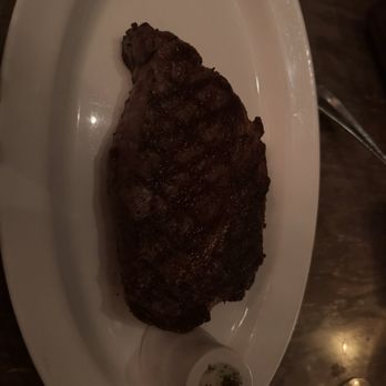 Mooo.... Beacon Hill - A cooked steak is presented on a white oval plate, accompanied by a small container of sauce with herbs. - Steakhouses Near Me - Boston, Massachusetts