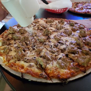 The Ding - Topped the hot pizza with  with parmesan cheese - A large pizza with sausage toppings is on a table, with parmesan cheese being sprinkled on top. - Bars Near Me - Wild Rose, Wisconsin