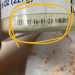 The Best By date - The image depicts a close-up of a food container with a printed expiration date of '26/01/23 11CB17'. The container appears to be partially visible, with some food residue or crumbs nearby. The focus is on the printed date, which is located at the bottom edge of the container.