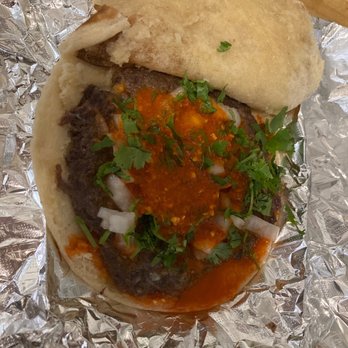 Barbacoa El Primo - A beef taco with chopped onions, cilantro, and red salsa on a soft tortilla, placed on aluminum foil. - Mexican Near Me - Albuquerque, New Mexico