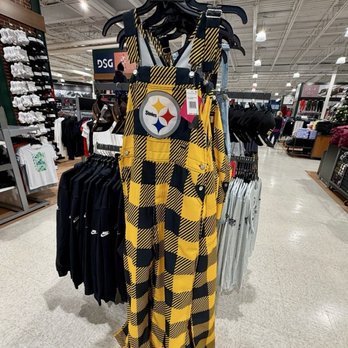 DICK'S Sporting Goods - Steelers overalls - Yellow and black plaid overalls featuring a Steelers logo are displayed on a clothing rack inside a retail store, surrounded by other apparel. - Sports Wear Near Me - Monaca, Pennsylvania