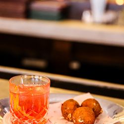 Felice Port Chester - A refreshing spritz-style cocktail in a textured glass sitting beside three golden-brown arancini served on branded Felice paper.