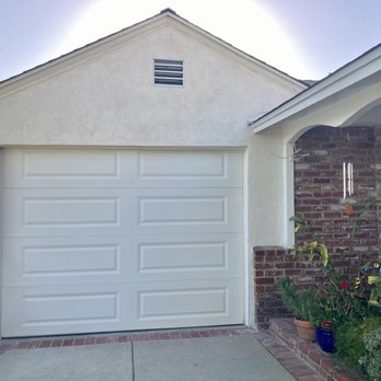 Carver's Plastering - A house features a white garage door, brick accents on the side wall, and a window with plants outside. The scene is outdoors during daytime. - Stucco Services Near Me