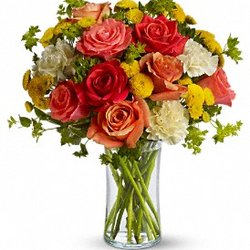 Dark orange, coral and orange roses, light yellow carnations, yellow button spray chrysanthemums and greens fill a slender gathering vase.