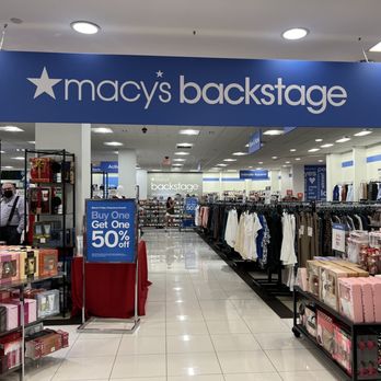 Macy's Backstage - Macy's Backstage is like a fancier Ross or Marshall's. It's where all the stuff people don't want go to die!!! Lol. - The image depicts the interior of Macy's Backstage retail store, featuring clothing racks with various apparel, gift and fragrance displays, and promotional signage. The store is well-lit with ceiling lights, and a large blue sign with white text reading 'macy's backstage' hangs above the entrance. Shelves and racks are organized, and a staff member wearing a mask is visible near the gift section. The store layout includes clear pathways and sections for different product categories. - Shoe Stores Near Me - Boca Raton, Florida
