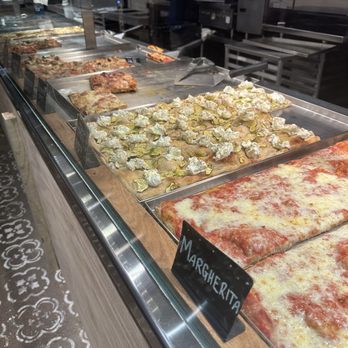 Bonci - The image features a glass display case containing several pizza slices and toppings, including a Margherita pizza with cheese and tomato sauce. The case is situated in a commercial kitchen or pizzeria setting, with kitchen equipment visible in the background. The display showcases a variety of pizza options, with some slices topped with ingredients like cheese, vegetables, and meats. - Pizza Near Me - Chicago, Illinois
