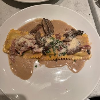 Aurora’s - Short Rib Ravioli Pasta - A white plate holds short rib ravioli pasta topped with mushroom slices, grated cheese, and garnished with herbs, served with a sauce. - Mediterranean Near Me - Fairfield, Connecticut