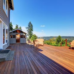 Decknology - A spacious wooden deck with a small shed and an elevated view of a rolling green landscape and hills in the distance, under a...