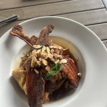 River & Post - Bacon and French toast - A white plate contains bacon, French toast, and chopped nuts, garnished with a small green herb, on a wooden table. - Lounges Near Me - Jacksonville, Florida
