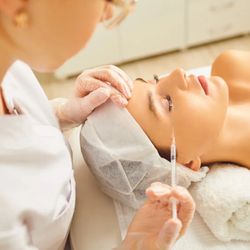 Ageless Beauty Center - A professional wearing glasses and white gloves is performing a cosmetic injection on a person's upper cheek, near the eye, a...