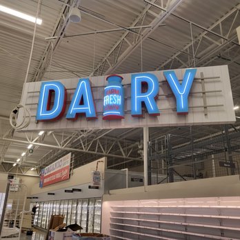 H-E-B - A neon sign reading 'DAIRY' with a milk bottle graphic is displayed inside a grocery store, above refrigerated sections and empty shelves. - Grocery Near Me - Magnolia, Texas