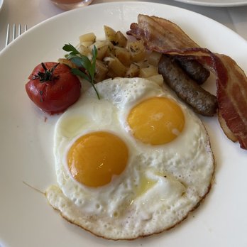 Orchids - Breakfast plate of two eggs sunny side up, breakfast potatoes with a roasted tomato, a strip of bacon and two sausage links. - Breakfast & Brunch Near Me - Honolulu, Hawaii Orchids - Breakfast plate of two eggs sunny side up, breakfast potatoes with a roasted tomato, a strip of bacon and two sausage links. - Breakfast & Brunch Near Me - Honolulu, Hawaii