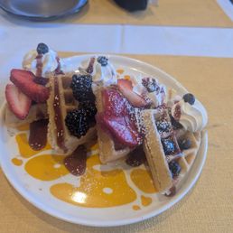 Mixed berries on top of some waffles top with some whipped cream.