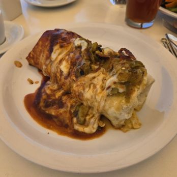 Dolina Santa Fe - Breakfast burrito. Christmas. - A breakfast burrito topped with green chili and sauce, served on a white plate at a restaurant table. - Cafes Near Me - Santa Fe, New Mexico