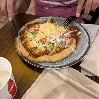 Black Mesa Casino - A person wearing a pink Reebok shirt is eating a taco salad topped with shredded cheese, lettuce, tomatoes, and meat at a restaurant. - Casinos Near Me - Algodones, New Mexico